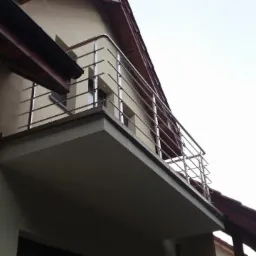 Balkon z nowoczesną, minimalistyczną balustradą ze stali nierdzewnej, widok z dołu, z elementami elewacji budynku.