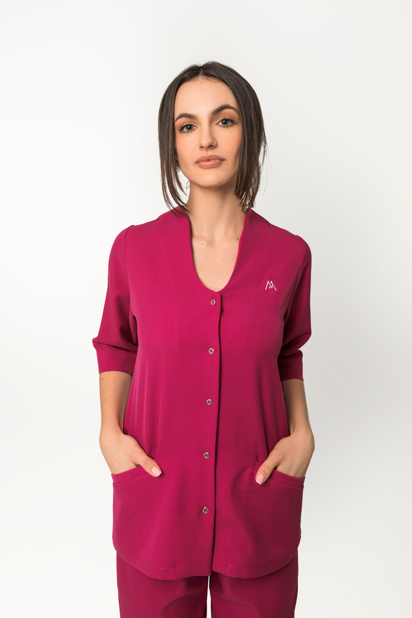 Kobieta w bordowym komplecie odzieży roboczej z kieszeniami, zapiętym na zatrzaski i z haftowanym logo na piersi, pozująca na białym tle.