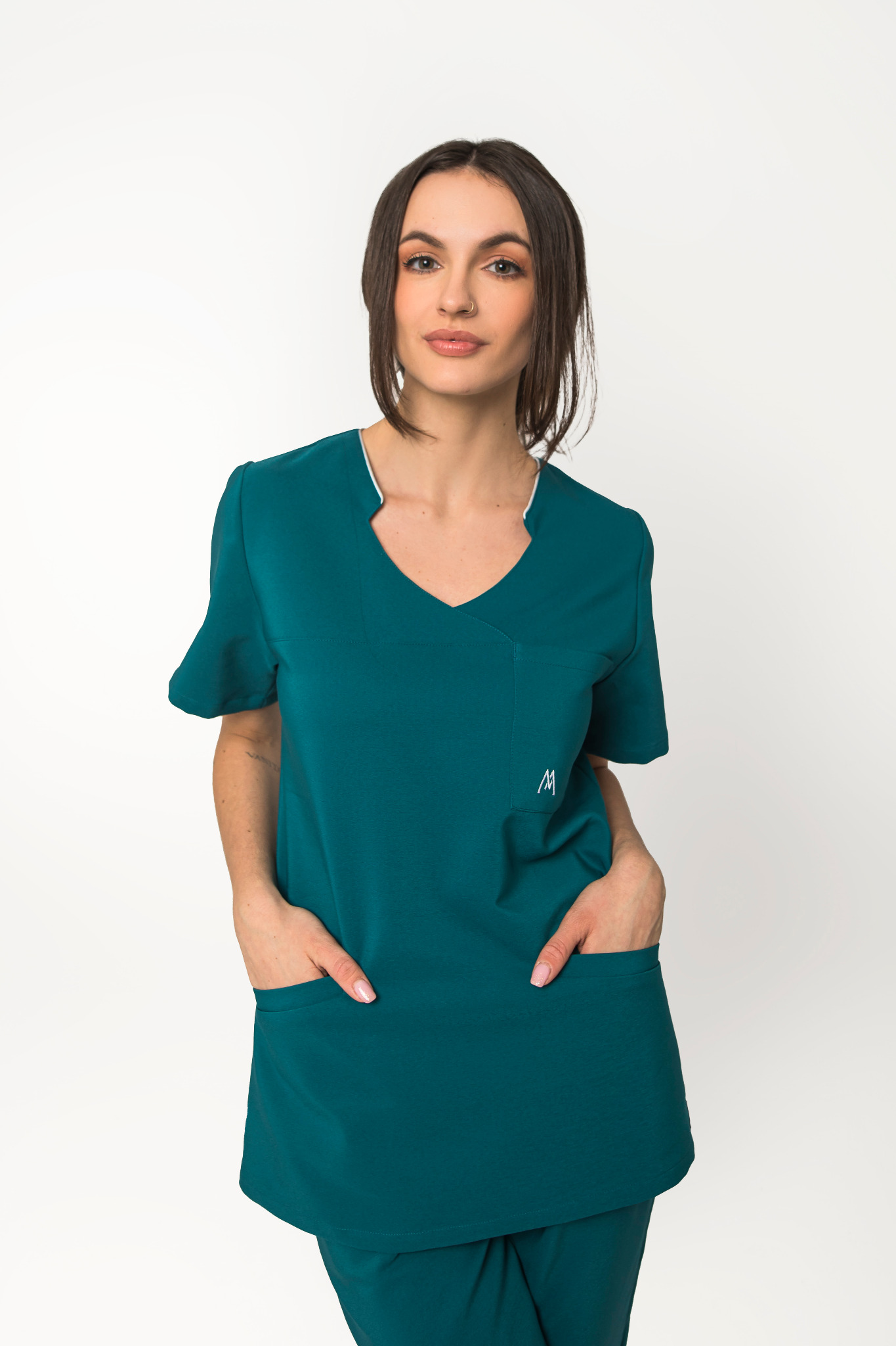 Kobieta w szmaragdowozielonym komplecie medycznym z krótkim rękawem i logo na kieszeni, pozująca na białym tle.