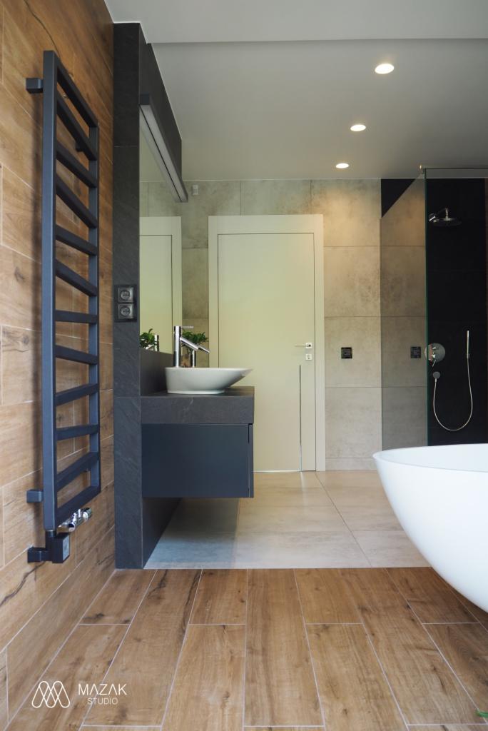 Nowoczesna łazienka z drewnopodobnymi płytkami, minimalistyczną umywalką nablatową i grzejnikiem drabinkowym w kolorze grafitowym.