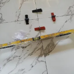 Położone płytki podłogowe imitujące marmur, z użyciem poziomicy i klipsów poziomujących, w trakcie prac wykończeniowych.