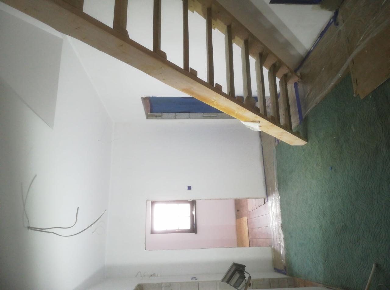 Wnętrze w trakcie odświeżania: świeżo pomalowane białe ściany, drewniane schody bez balustrady, zabezpieczona folią podłoga i widoczne kable elektryczne.