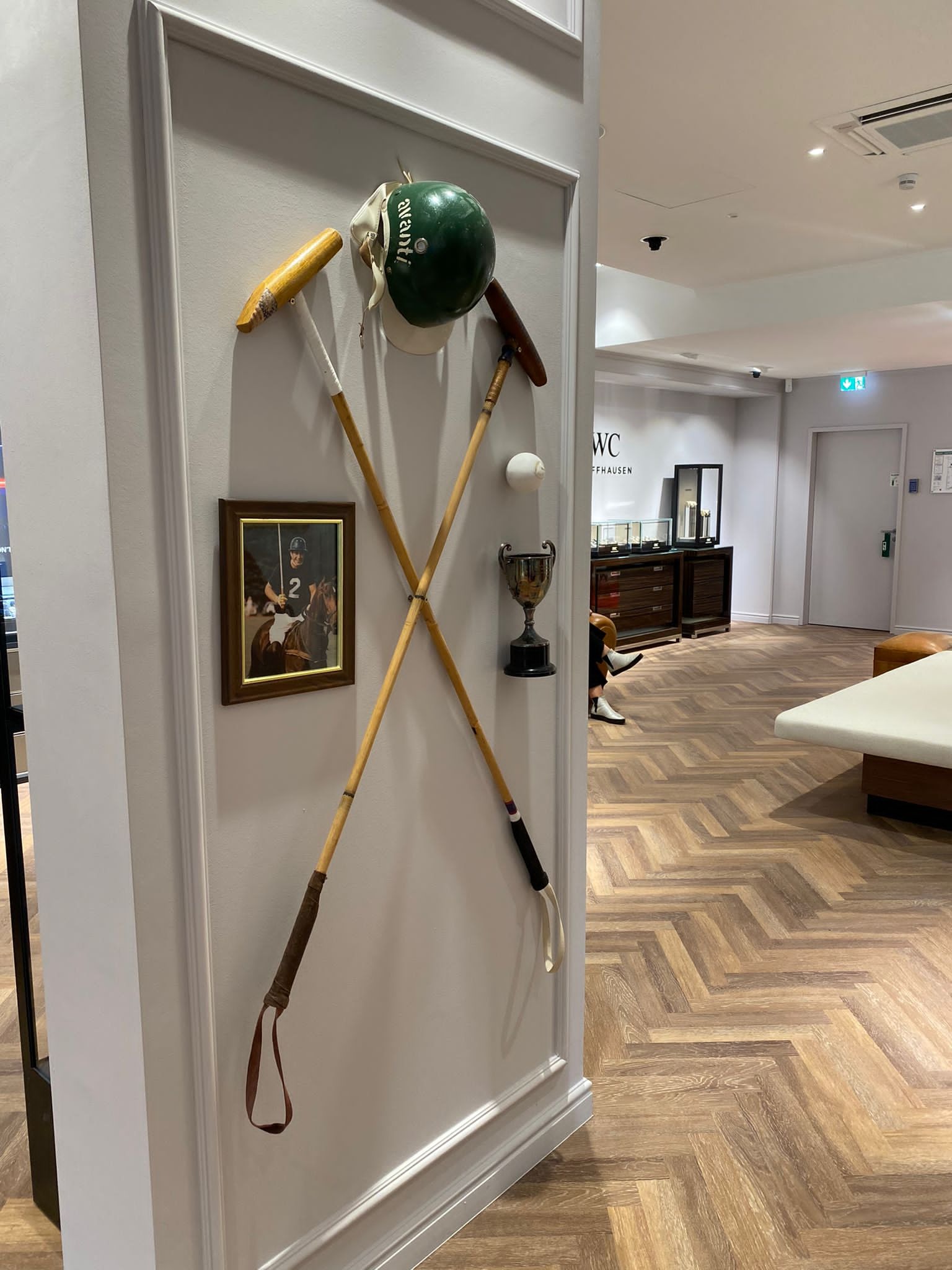 Dekoracja ścienna w sklepie: skrzyżowane kije do polo, zielony kask jeździecki, piłka, trofeum i oprawiony portret jeźdźca na koniu.