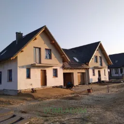 Budowa osiedla: szereg domów jednorodzinnych w zabudowie bliźniaczej w trakcie prac wykończeniowych. Okna zabezpieczone folią, widoczne materiały budowlane i narzędzia.