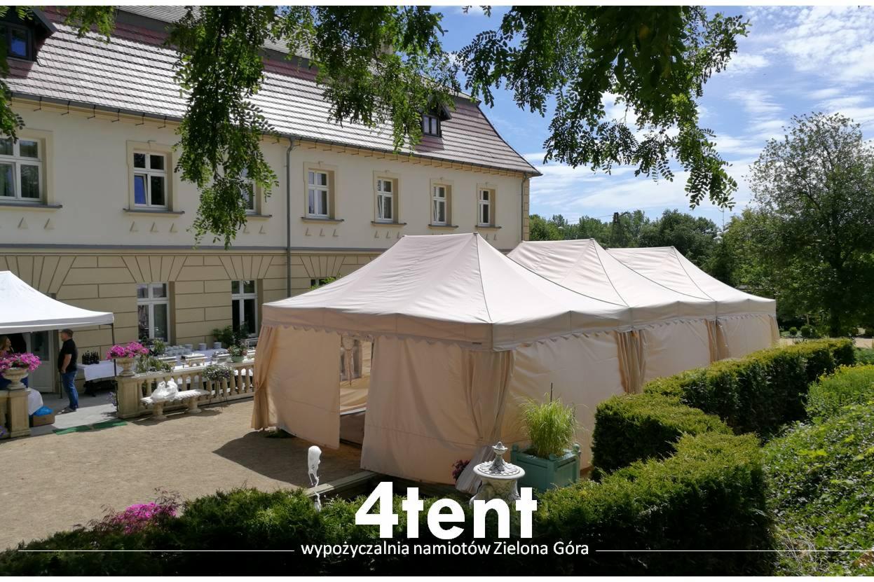 Rozstawione beżowe namioty bankietowe z firanami na zewnątrz budynku, widoczne stoły z zastawą i kwiatami.