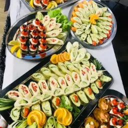 Elegancko ułożone na srebrnych tacach przekąski: roladki z tortilli z warzywami, koreczki z pomidorkami cherry i mozzarellą, dekorowane cytrusami i zieleniną.