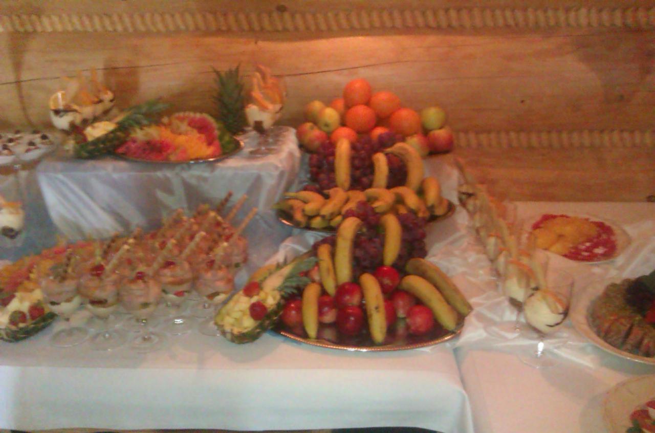 Stół z owocami, deserami i przystawkami podczas uroczystości, drewniane panele w tle.