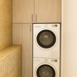 Sylwestri Usługi remontowo-budowlane - Zabudowa pralki i suszarki w łazience z beżowymi szafkami podwieszanymi i ścianą z cegieł w ciepłym odcieniu. Minimalistyczny design i funkcjonalne rozwiązanie do małych przestrzeni.