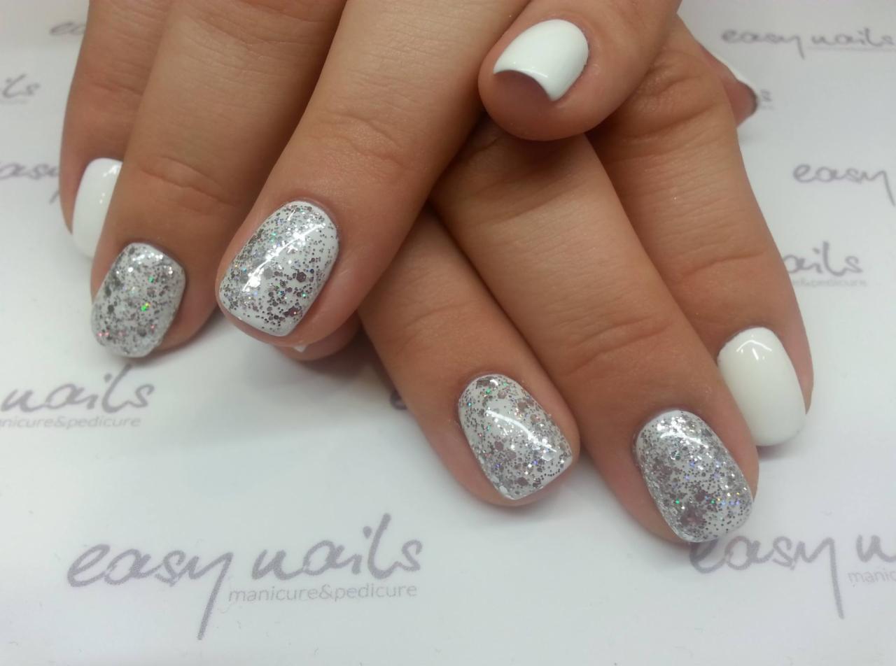 Dłoń z pomalowanymi paznokciami: trzy srebrne brokatowe i dwa białe, na białym tle z logo salonu kosmetycznego.