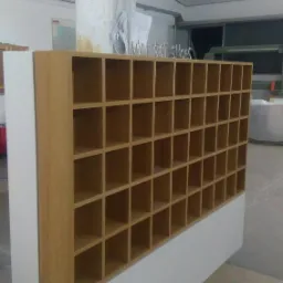 Drewniana szafka na buty z wieloma przegródkami, umieszczona w warsztacie, z napisem 'MY FIRST SHOES' na górze.