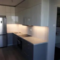 Nowoczesna kuchnia z szarymi dolnymi szafkami i białymi błyszczącymi górnymi szafkami, podświetlona listwą LED, z widoczną płytą indukcyjną i piekarnikiem.