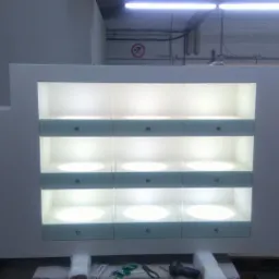 Biała lada sklepowa z podświetlanymi półkami i szufladami, widoczna w hali produkcyjnej, częściowo zapakowana do transportu.