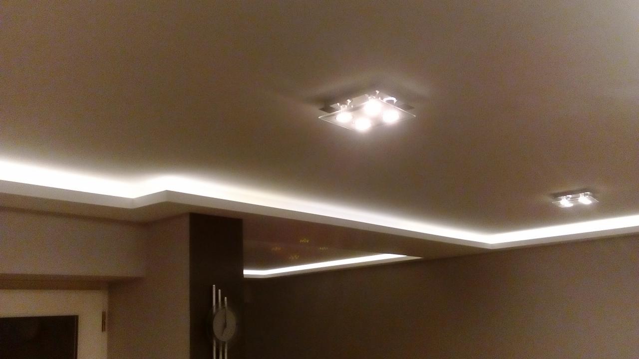 Sufit podwieszany z oświetleniem LED i lampą kwadratową z czterema żarówkami, widoczny fragment ściany z zegarem.