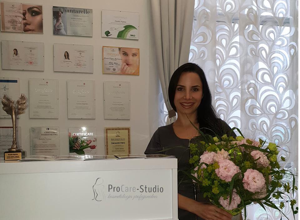 Uśmiechnięta kobieta z bukietem kwiatów w recepcji, na ścianie certyfikaty i nagrody, widoczne logo ProCare-Studio kosmetologia profesjonalna.