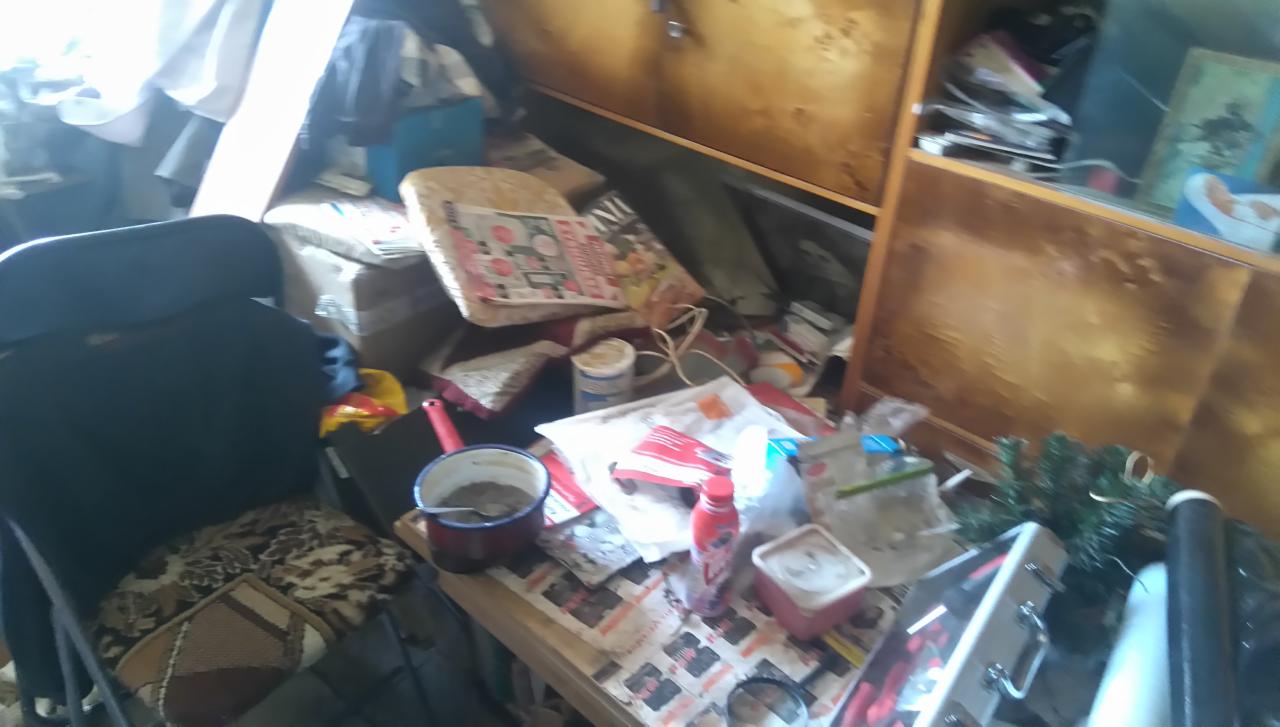 Zabałaganione pomieszczenie z różnymi przedmiotami, w tym krzesłem, szafką, garnkiem i różnymi opakowaniami, sprawiające wrażenie zaniedbanego i wymagającego sprzątania.