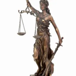 Brązowa statuetka Temidy z zasłoniętymi oczami, trzymająca wagę i miecz, stojąca na książkach i wężu, na białym tle.