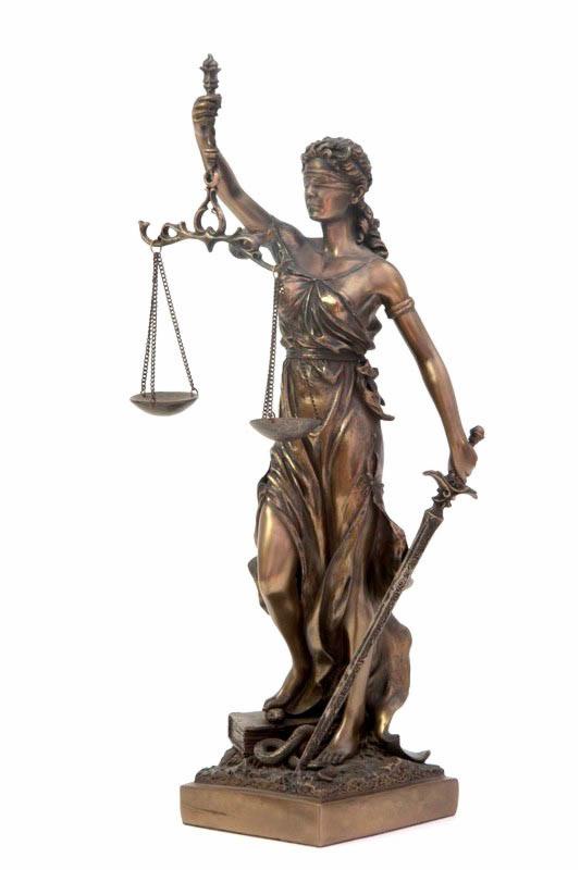 Brązowa statuetka Temidy z zasłoniętymi oczami, trzymająca wagę i miecz, stojąca na książkach i wężu, na białym tle.