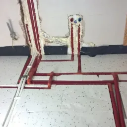 Instalacja ogrzewania podłogowego z czerwonymi rurami, zalewana pianką montażową w ścianach, widoczne białe płyty styropianowe z czarnymi kropkami na podłodze i czarna folia przy ścianie.