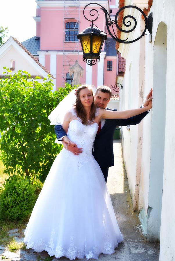 Para młoda w objęciach na tle różowego budynku z białą kolumnadą i ozdobną latarnią.