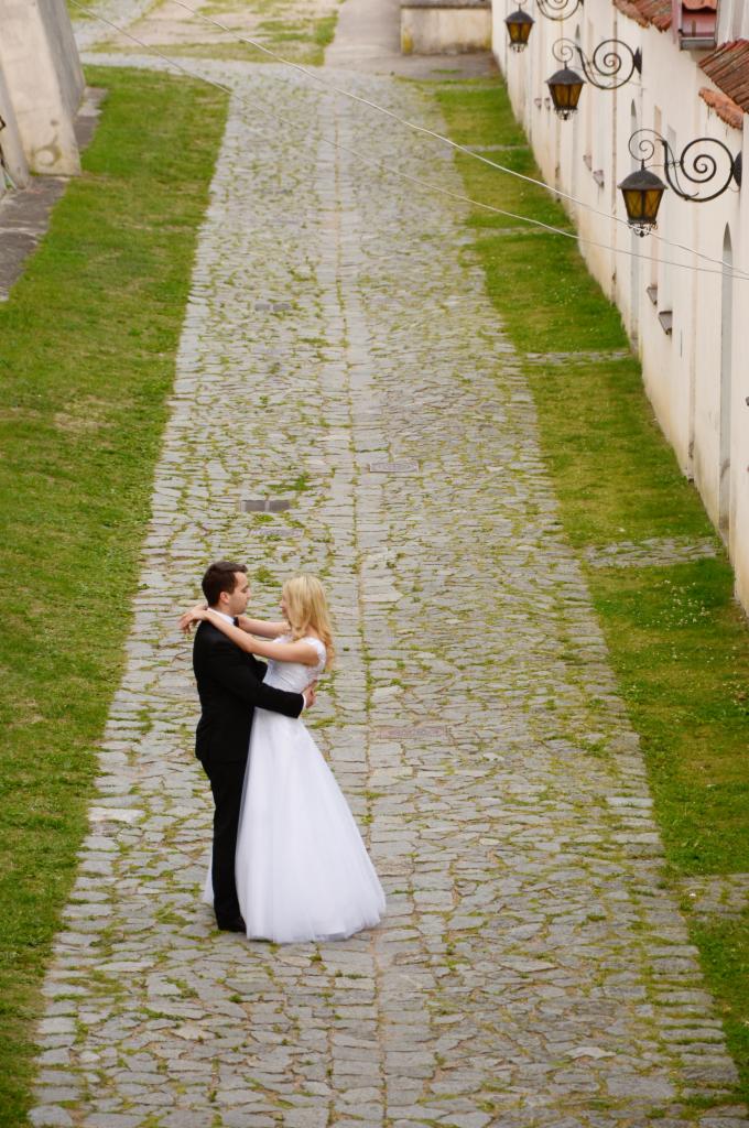 Para młoda obejmuje się na brukowanej drodze w historycznym otoczeniu z ozdobnymi latarniami, widok z góry.