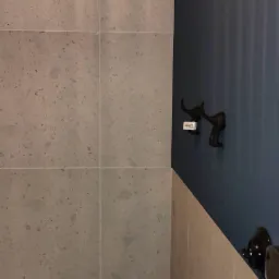 Fragment wykończonej łazienki z szarą, nakrapianą glazurą na ścianach, kontrastującą z granatową ścianą, na której wiszą wieszaki w kształcie głowy słonia oraz widoczny fragment czarno-białej...