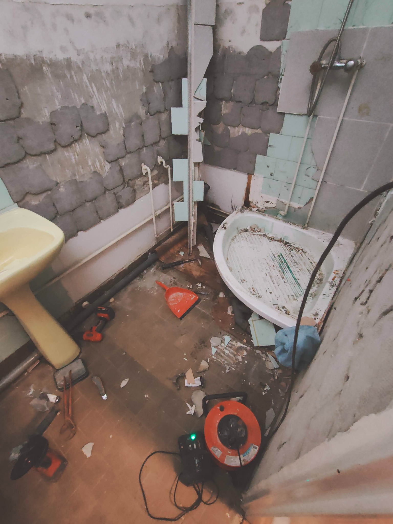 Demontaż starej łazienki: widoczne niedokończone ściany z resztkami płytek, odłączona wanna i umywalka, narzędzia i gruz na podłodze.