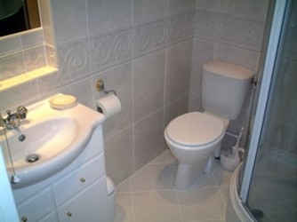 Jasna łazienka po remoncie: biała ceramika, umywalka z szafką, toaleta kompaktowa, płytki ścienne z delikatnym wzorem, widoczny fragment kabiny prysznicowej.