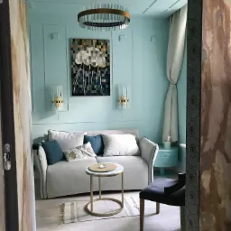 Turkusowy gabinet z sofą, okrągłym stolikiem kawowym, abstrakcyjnym obrazem meduzy i lampami ściennymi w stylu art deco.