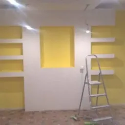 Żółto-biała ściana z wnękami i półkami w trakcie wykończenia, widoczne drabiny malarskie i niedokładności malowania.