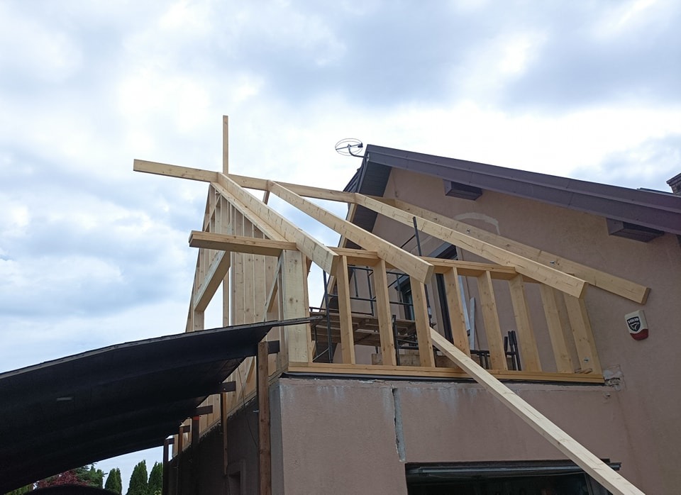 Konstrukcja drewniana dobudowywana do istniejącego budynku z widocznym fragmentem dachu i alarmem.