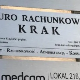 Metalowa tabliczka informacyjna na ścianie budynku z napisem 'BIURO RACHUNKOWE KRAK' oraz adresem, numerem telefonu i adresem e-mail. Poniżej widnieją napisy: KADRY - RACHUNKOWOŚĆ - ADMINISTRACJA -...