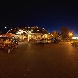 Fotografia Mariusz Olszowski - Panoramiczne ujęcie oświetlonego nocą Gościńca Kanclerz z zaparkowanymi samochodami i firmowym vanem z reklamą, widok z kostki brukowej.