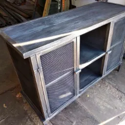 Metalowa szafka RTV z siatką, surowy industrialny styl, widoczne spawy i łączenia, ciemne wykończenie drewna na blacie i półkach.