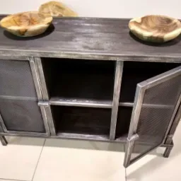 Metalowa komoda z siatkowymi drzwiczkami, jedna z nich otwarta, na blacie dwie drewniane misy, styl industrialny.