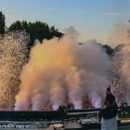 DJ na scenie z konfetti i dymem podczas występu dla tłumu, oświetlenie sceniczne w tle.