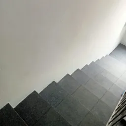 Schody wyłożone ciemnoszarymi, granitowymi płytkami, widok z góry, przylegające do białej ściany.