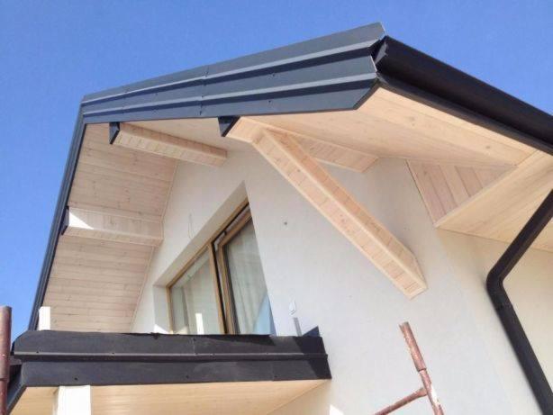 Fragment nowo wybudowanego domu z widoczną konstrukcją drewnianą okapów, blachą na dachu i rynnami w kolorze czarnym.
