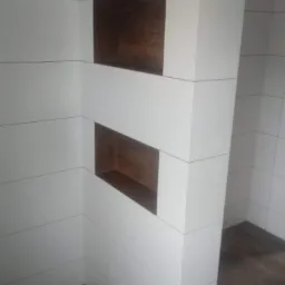 Białe, prostokątne płytki ścienne z ciemnobrązowymi wnękami w ścianie, uzupełnione podłogą z paneli imitujących drewno.