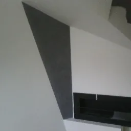 Ściana z fragmentem pomalowanym na szaro tworzącym geometryczny wzór, obok czarny prostokątny element dekoracyjny wnęki.