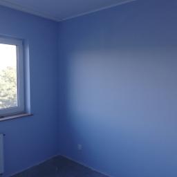 usługi malarskie Marcel - Świeżo pomalowany pokój w odcieniach błękitu, widoczne okno z widokiem na zieleń, biały grzejnik oraz gniazdko elektryczne przy podłodze.