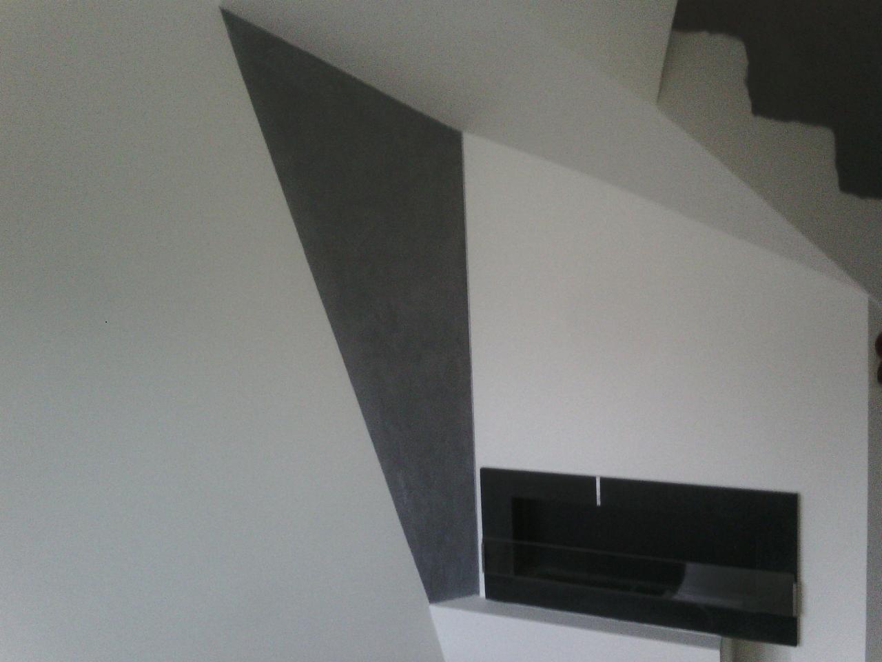 Ściana z fragmentem pomalowanym na szaro tworzącym geometryczny wzór, obok czarny prostokątny element dekoracyjny wnęki.