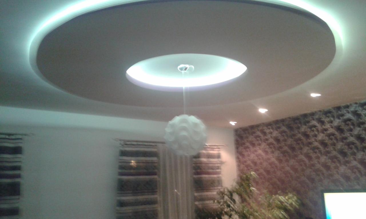 Okrągły sufit podwieszany z oświetleniem LED i wiszącą lampą kulą, widoczne fragmenty ścian w kolorze białym i z wzorzystą tapetą.