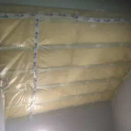 Poddasze w trakcie ocieplania, widoczne belki konstrukcyjne, izolacja pokryta folią i zabezpieczona taśmą z logo Rigips, przygotowane do montażu płyt.