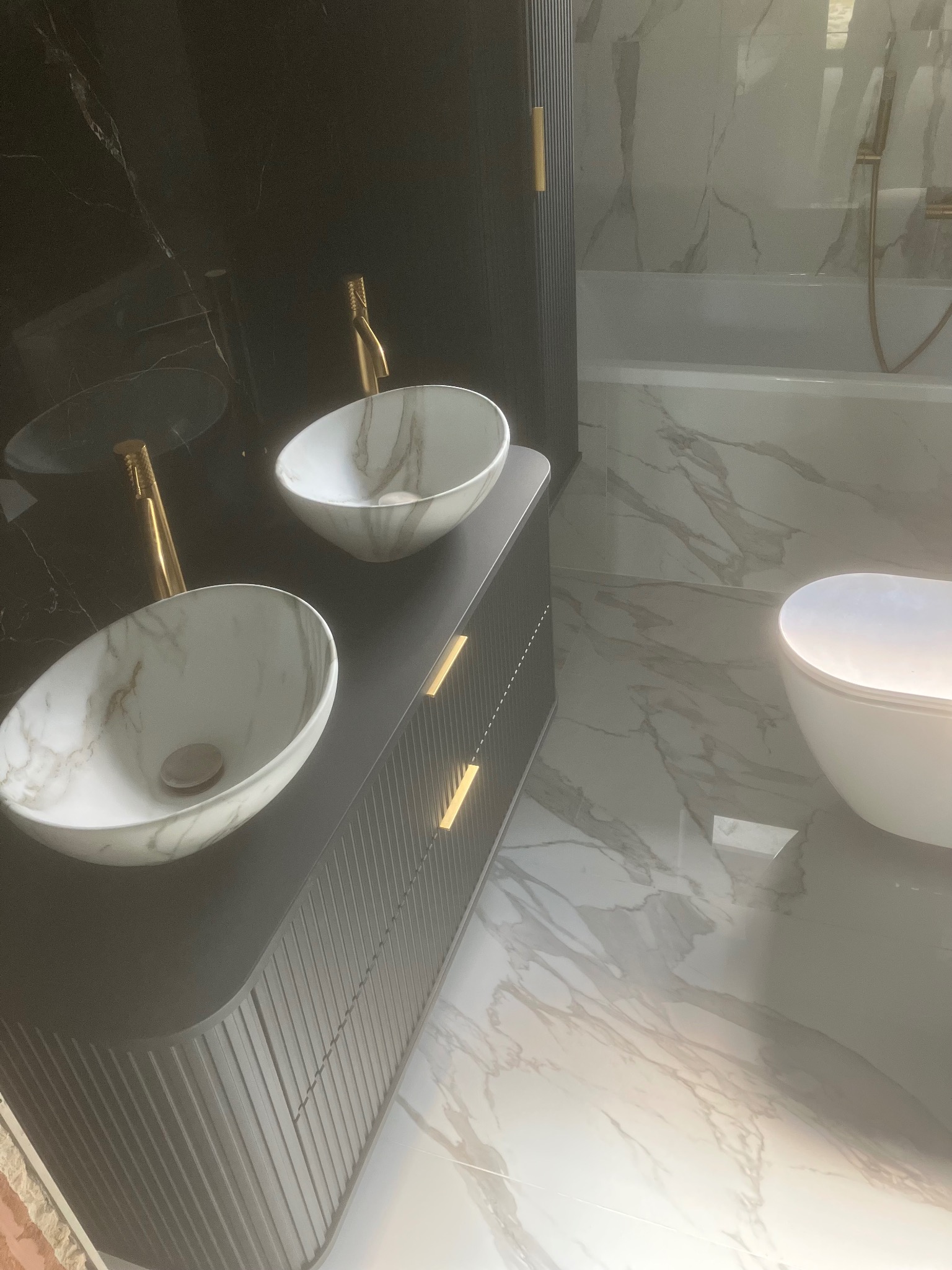 Nowoczesna łazienka z marmurowymi płytkami, umywalkami nablatowymi w odcieniach bieli i złota armatura. Minimalistyczny design i eleganckie wykończenie.