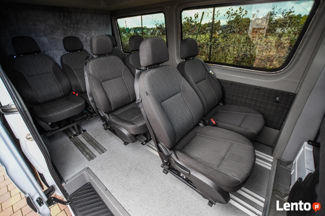 Wnętrze busa z czarnymi fotelami pasażerskimi na szynach, widok z otwartych drzwi.