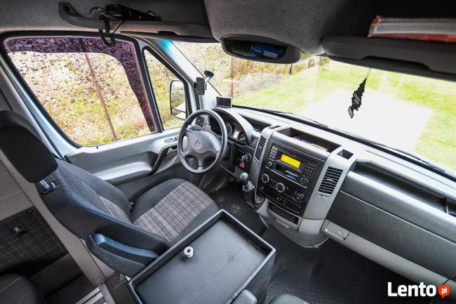 Wnętrze busa marki Mercedes z widocznym kokpitem, kierownicą i fotelami w kratę, z zawieszką zapachową na desce rozdzielczej.