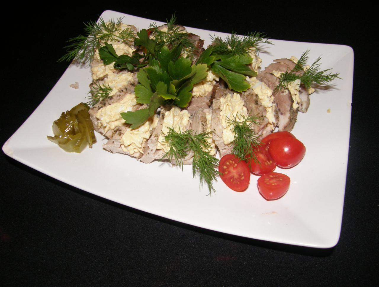 Plasterki mięsa z sosem jajecznym, udekorowane koperkiem i natką pietruszki, podane na białym kwadratowym talerzu z dodatkiem pomidorków cherry i korniszonów.