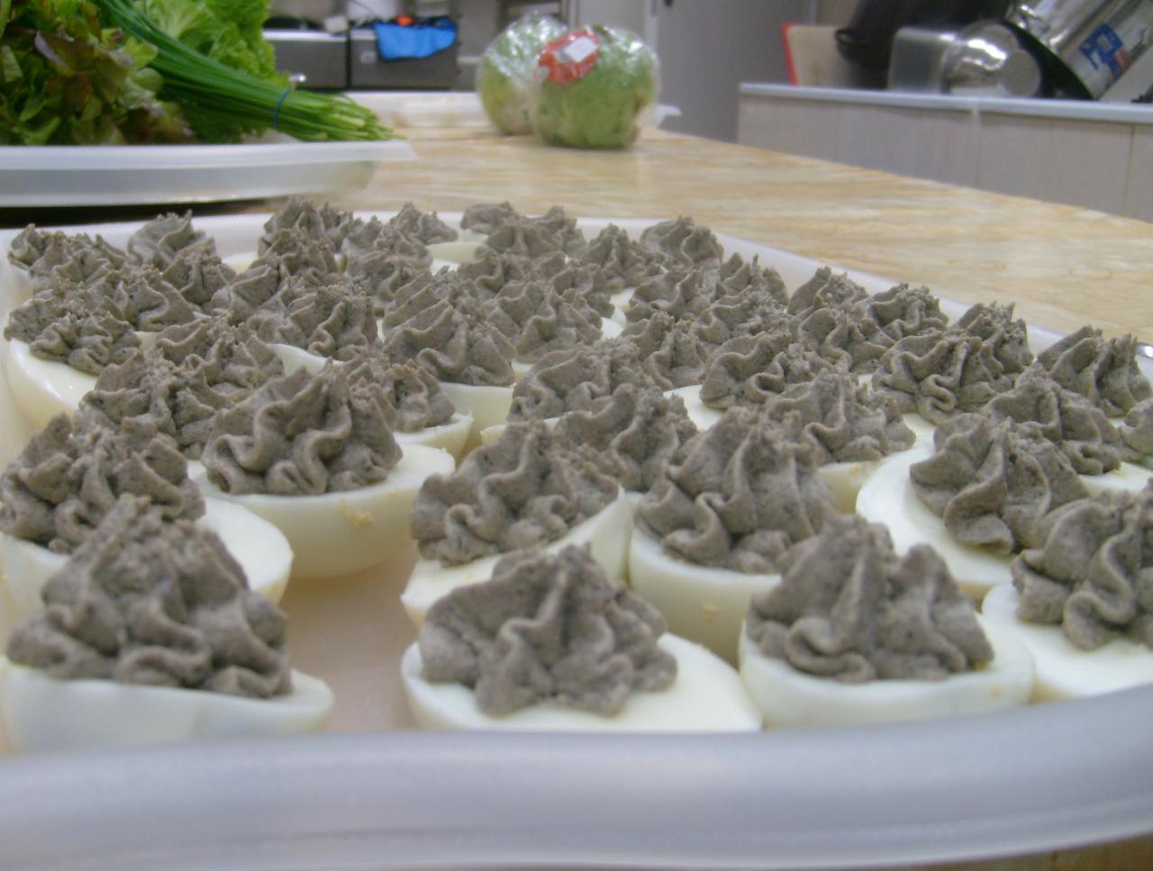 Taca z faszerowanymi jajkami, udekorowanymi ciemnoszarą pastą, z zieloną sałatą i szczypiorkiem w tle, gotowe do serwowania.