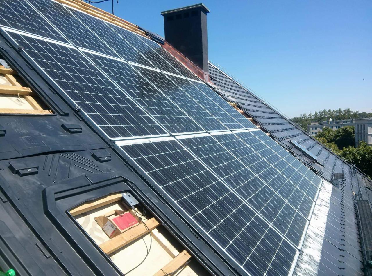 Panele słoneczne zamontowane na dachu domu z widocznym kominem i fragmentem instalacji elektrycznej w otworze dachu.