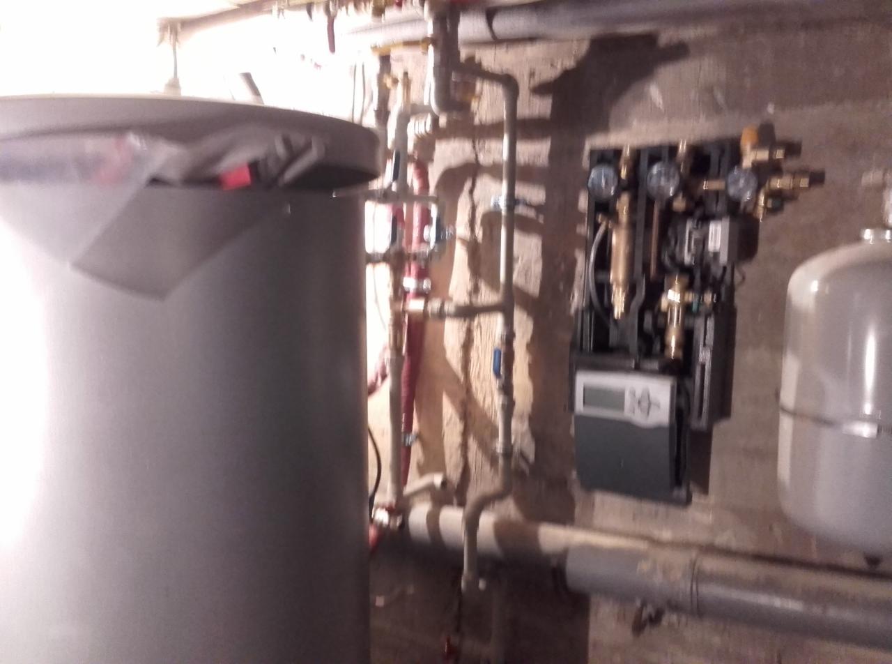 Instalacja centralnego ogrzewania z kotłem, rurami, zaworami i sterownikiem na ścianie z betonu komórkowego. Widoczne również naczynie przeponowe.